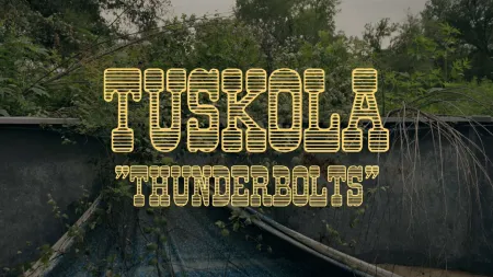 Yellow Tuscola Thunderbolts text over a dark, overgrown outdoor background with trees and weeds.