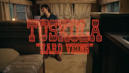Man sitting in a vintage RV with large red text Tuscola Hard Veins over the image.