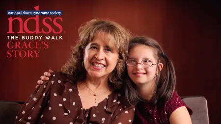 Smiling woman and young girl with Down syndrome sitting together for National Down Syndrome Society Buddy Walk event.