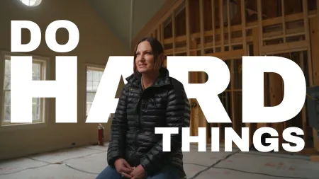 Woman in black jacket sitting in an unfinished room with bold text saying Do Hard Things in background