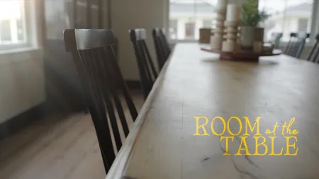 Empty wooden dining table with chairs bathed in natural light and text Room at the Table on surface.