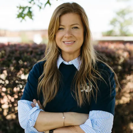 Confident woman with long hair in casual attire standing outdoors with arms crossed.