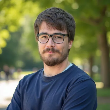 Young man with glasses and beard wearing a navy blue sweater standing outdoors with arms crossed