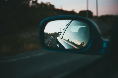 Car side mirror reflecting a road and telephone poles during sunset with approaching headlights.