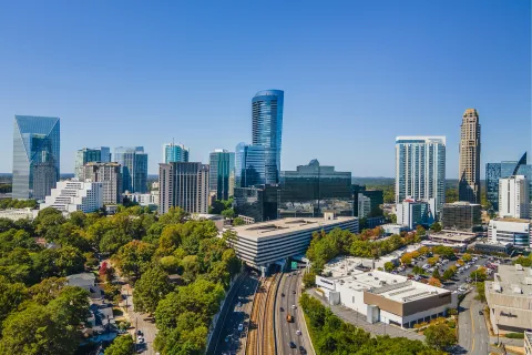 Aerial view of Atlanta city skyline with modern skyscrapers, green trees, and busy roads on a clear day