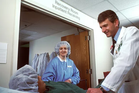 Doctor and nurse attending to a patient in a hospital recovery room, showing medical care and support.
