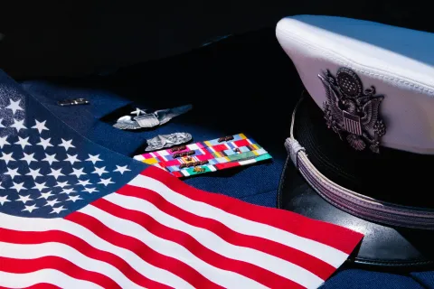 United States Navy officer's uniform with rank insignia, ribbons, American flag, and white service cap.