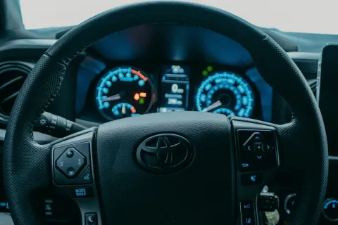 View of a Toyota steering wheel and dashboard with rain drops on the windshield in a parked car.
