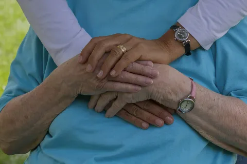 Close-up of two people embracing with hands gently clasped, showing care and support.