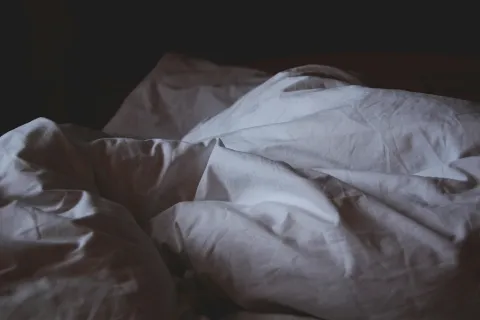 Crumpled white bed sheets and pillows in dim lighting on an unmade bed.