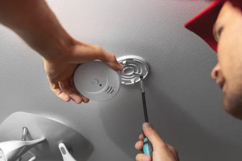 Technician installing a CO detector on a ceiling using a screwdriver.