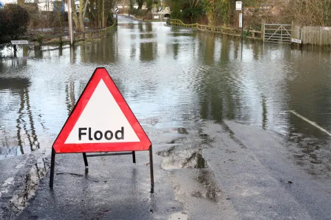 Flood warning sign on a water-covered road during heavy flooding with trees and fences in the background