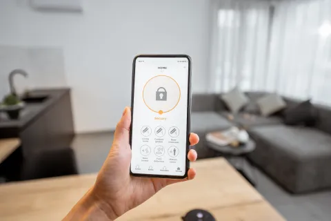 Hand holding smartphone displaying a home security app interface with locked status in a modern living room.