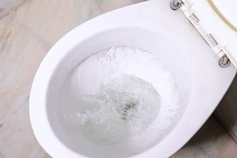 Top view of a white toilet bowl flushing with water swirling inside on marble floor.