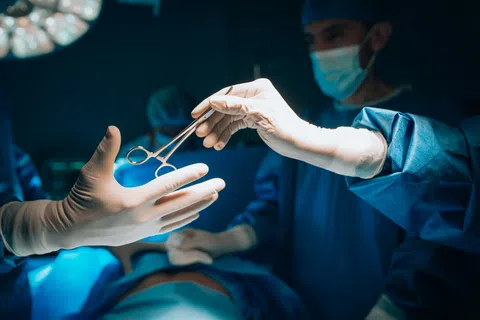Surgeons in sterile gloves passing surgical instrument during operation in hospital operating room.
