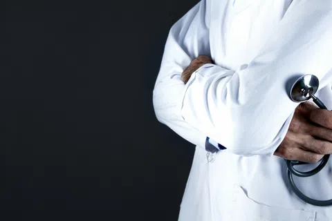 Doctor in white coat holding a stethoscope with arms crossed against a dark background