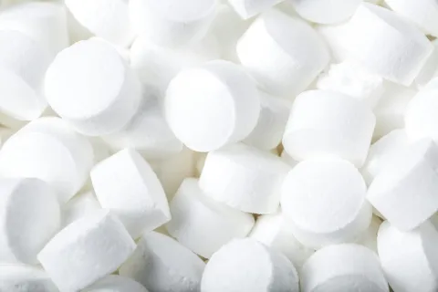 Close-up of many small white round tablets or pills piled together with smooth surfaces.