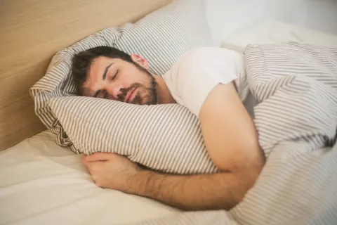 Man peacefully sleeping on bed hugging striped pillow with matching striped duvet in bright room