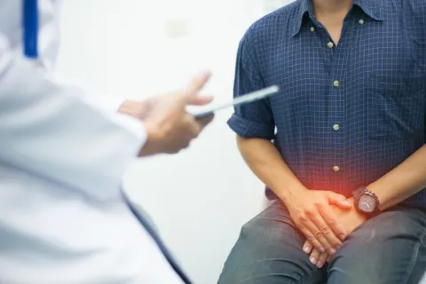 Man in blue shirt with hands on lower abdomen showing pain during a medical consultation with doctor.