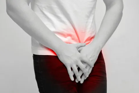 Person in white shirt and dark pants holding lower abdomen with red highlight indicating pain