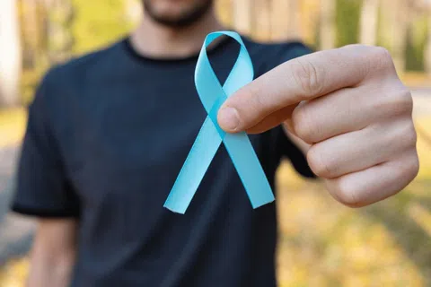 Man holding a blue ribbon symbol, representing prostate cancer awareness outdoors on a blurred background.