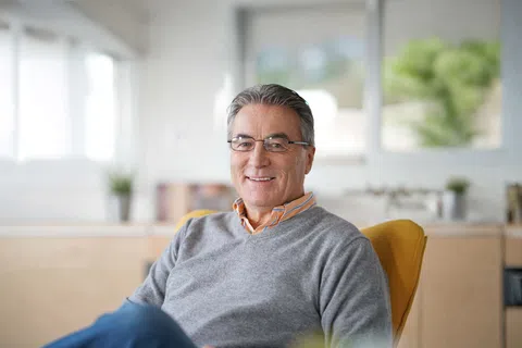 Smiling middle-aged man wearing glasses and grey sweater sitting comfortably in a bright modern office.