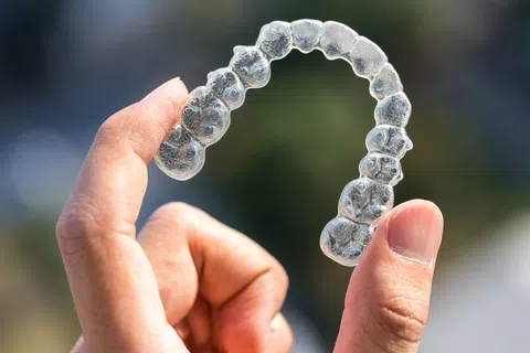 Hand holding a clear dental aligner or retainer against a blurred outdoor background.