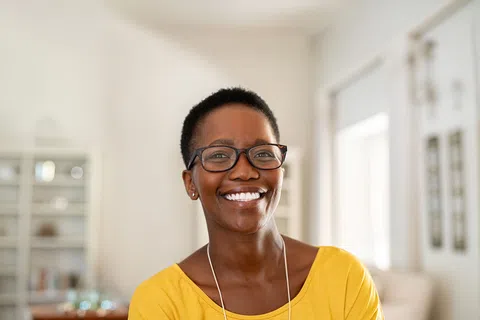 Smiling woman with short hair and glasses wearing a yellow top in a bright, modern room.