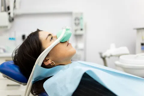 Woman reclining in dental chair wearing nitrous oxide mask and dental bib during treatment.