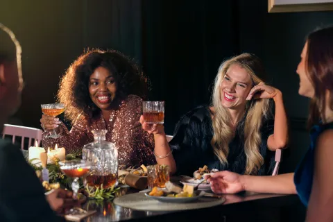 Group of friends enjoying drinks and food, smiling and toasting at a festive dinner party.