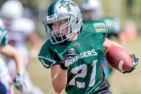 Youth football player in green Rangers jersey running with ball during game