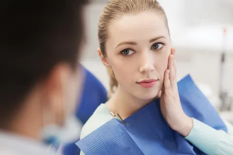 Young woman at dentist appointment holding her cheek, concerned about dental pain or examination.