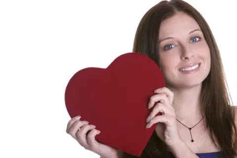 Smiling woman with blue eyes holding a large red heart shape against white background