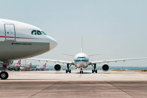 Two commercial airplanes on a runway, one facing forward and the other showing side view with clear sky above.