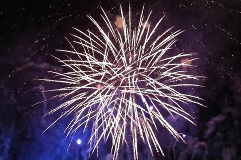 Bright white fireworks exploding in the night sky with purple smoke and dark background