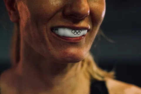 Close-up of athlete smiling with white mouthguard featuring Olympic rings logo