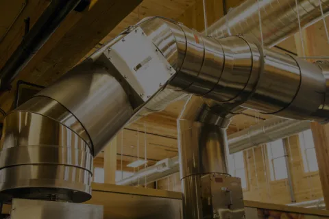 Stainless steel industrial ventilation ducts in a modern wooden ceiling building interior with natural light.