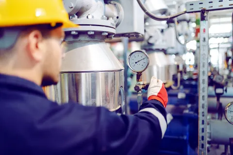 Engineer in yellow helmet checking pressure gauge on industrial machinery in factory setting