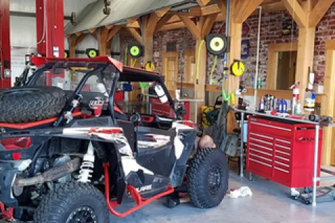 Off-road vehicle with large tires in a garage workshop with red tool chest and wooden beams