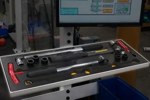 Tray of torque wrenches and sockets displayed on a workstation with a computer monitor in the background.