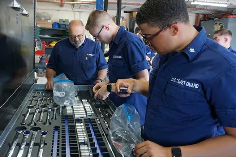 U.S. Coast Guard personnel sorting and organizing tools in a maintenance workshop for equipment readiness