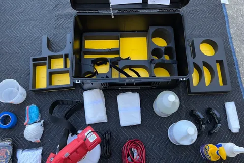 Open black equipment case with yellow inserts surrounded by automotive detailing tools and cleaning supplies on black mat.