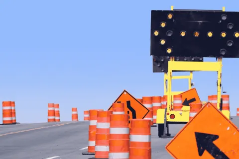 Roadwork zone with orange traffic barrels, directional arrow signs, and electronic arrow board on a clear day.