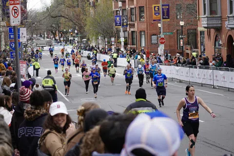 Runners participating in a marathon race on city streets with spectators and police presence.