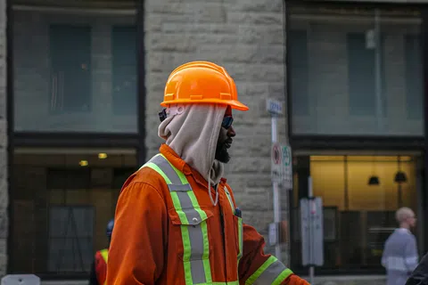 Construction worker in orange safety gear and helmet fist bumping another person on urban street.