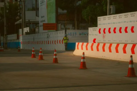 Construction zone with orange traffic cones and white barriers with red arrows in an urban area.