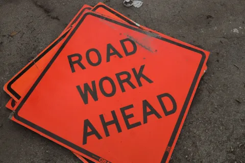 Bright orange road work ahead signs stacked on asphalt surface with black text.