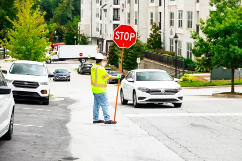Construction worker in safety vest holding stop sign directing traffic on urban street near parked cars