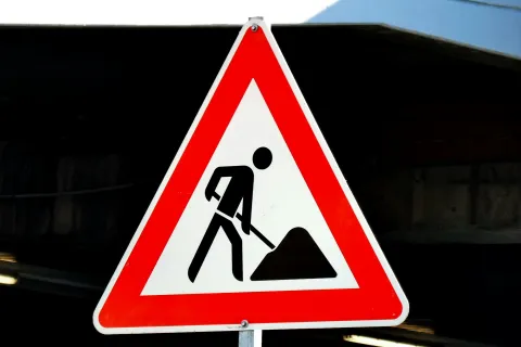 Red and white triangular road sign showing a worker digging, indicating construction or road work ahead.