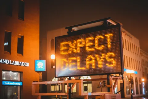 Electronic road sign lit at night displaying the message Expect Delays in an urban area.